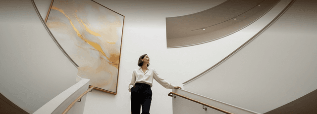 Woman in business attire examining artwork in a modern spiral staircase gallery. Human image in this ad was created using AI.