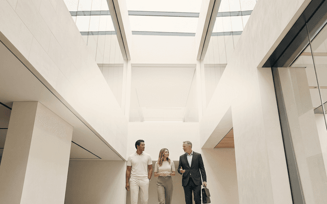 Three professionals engaged in conversation in a minimalist interior with natural skylight. Human images in this ad were created using AI.